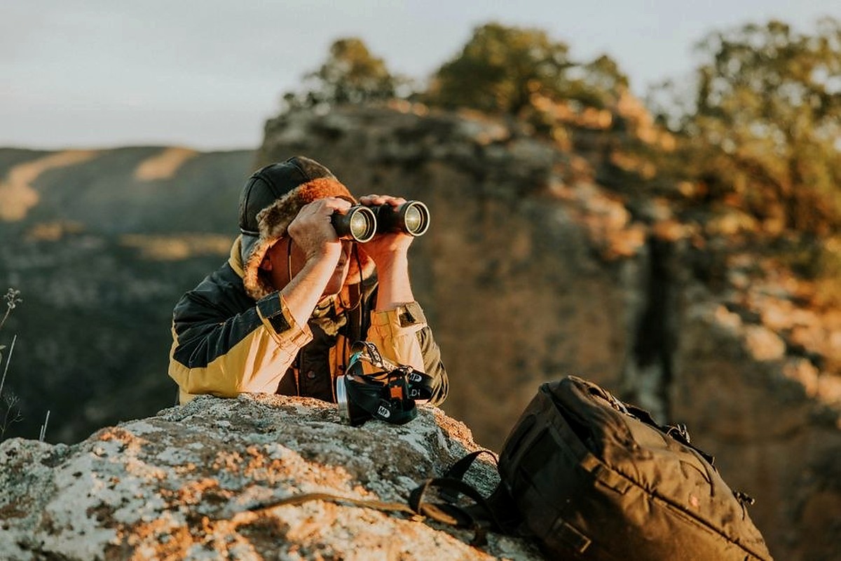 Photographer with a camera pausing on a rocky hillside above the landscape