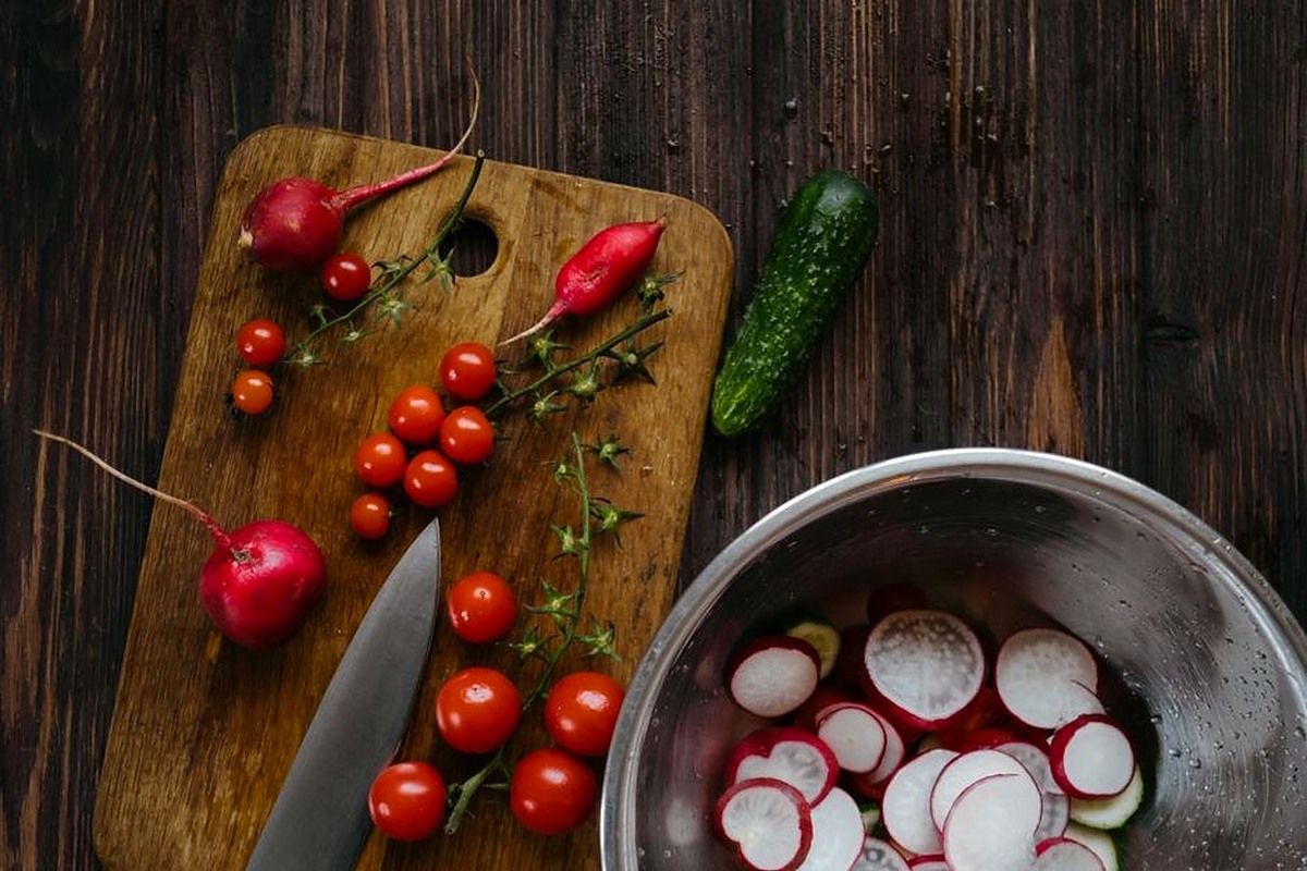 Fresh radishes tomatoes and cucumber arranged on a wooden kitchen table